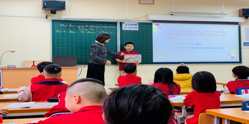 A person standing in front of a classroom with a child in red shirts

Description automatically generated